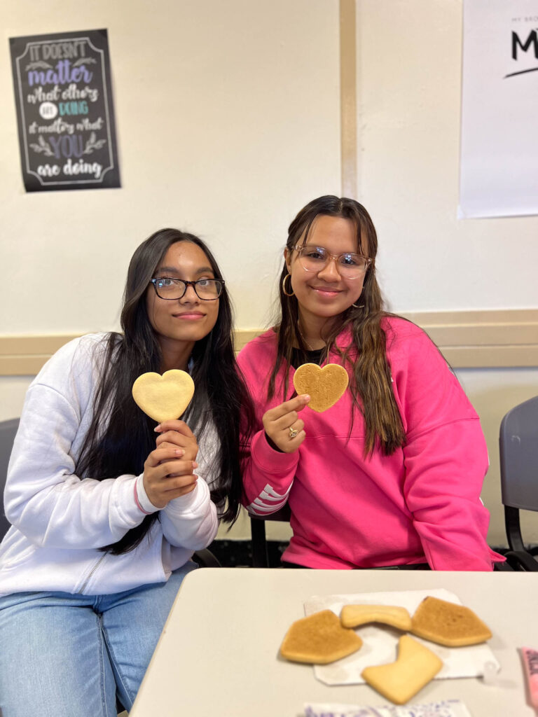 Two women sitting at a table holding heart shaped cookies.