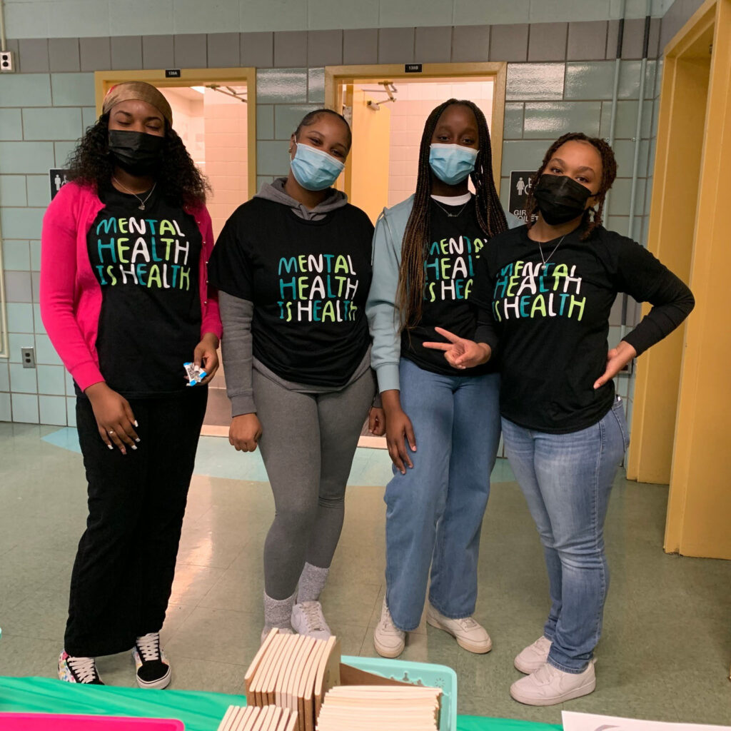 Four women wearing masks standing in front of a table.